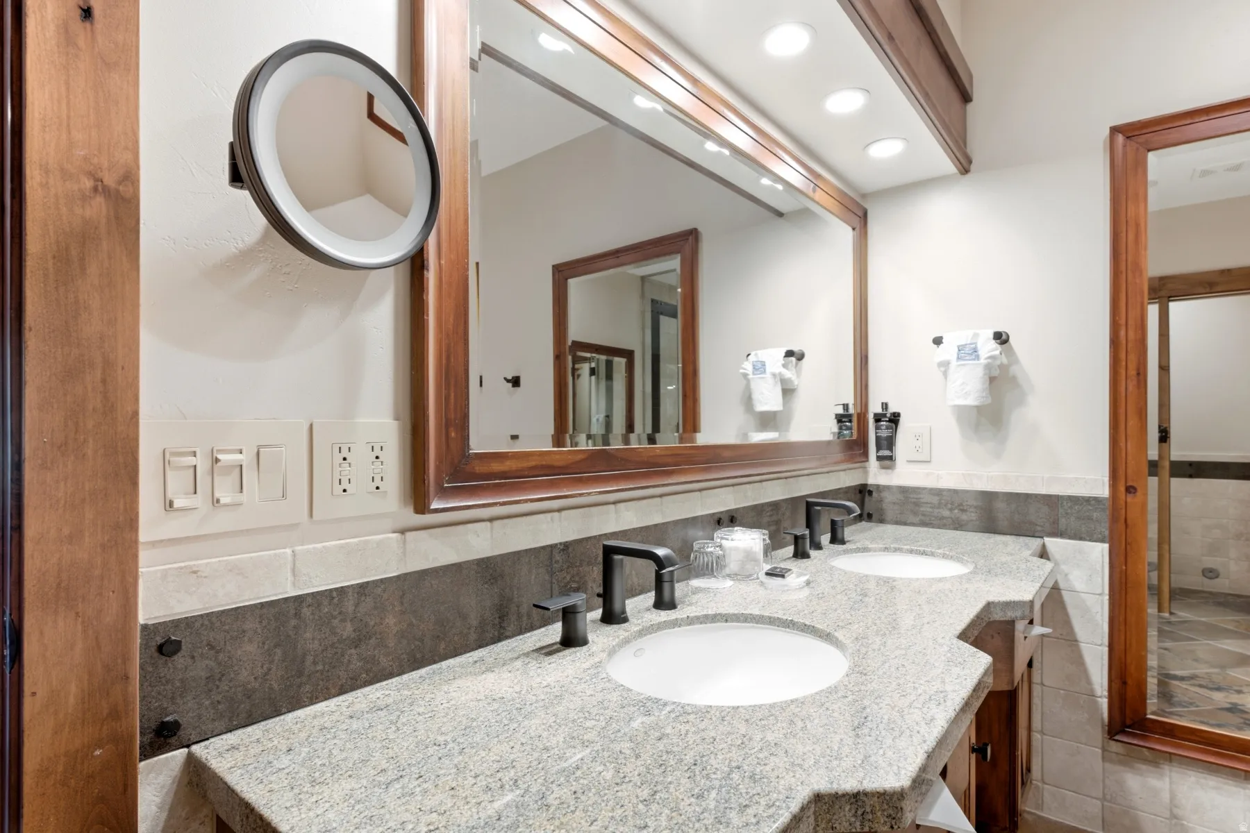 Bathroom vanity featuring a dual sink design with matte black fixtures, a granite-finish countertop, and an expansive wood-framed mirror
