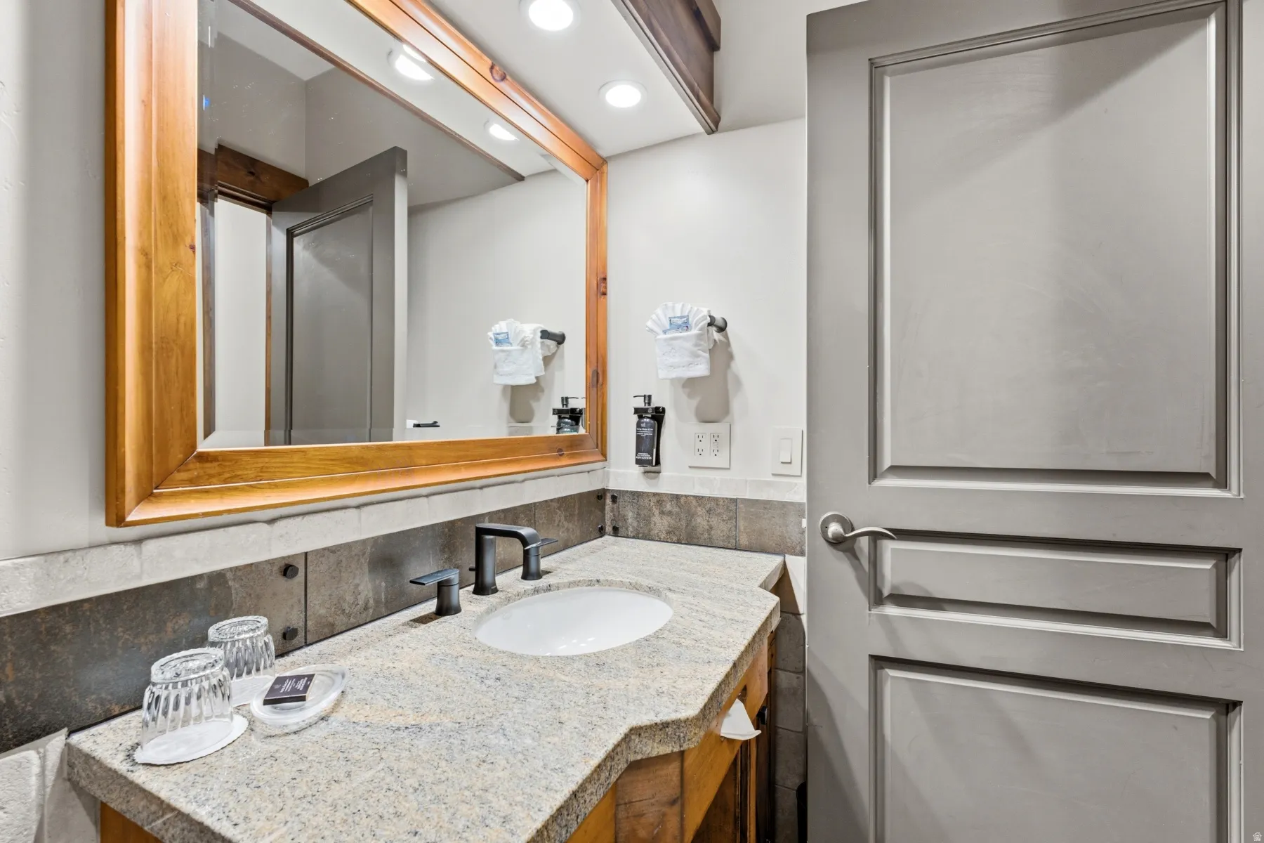 Bathroom vanity featuring a light granite countertop, undermount sink, and matte black faucet