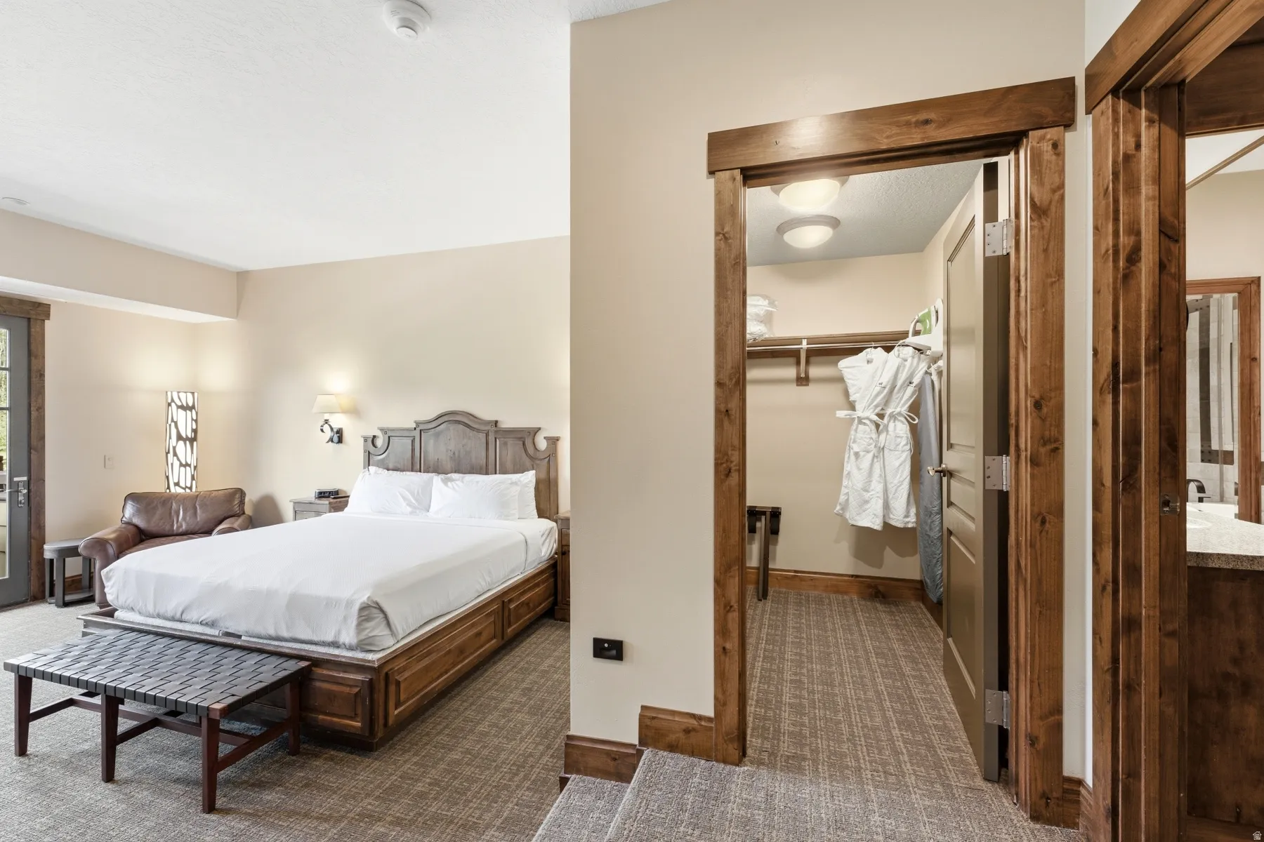 Carpeted sleeping area with a wood-finish bed frame, an adjacent walk-in closet with built-in shelving, and a vanity space with a stone-finish countertop