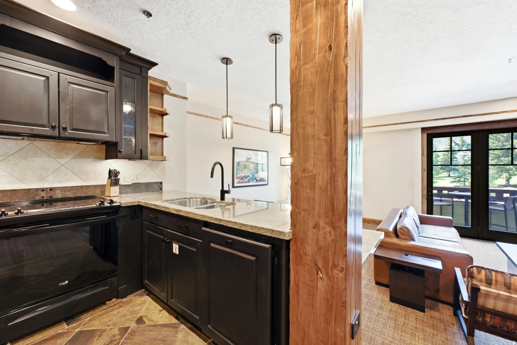 Compact kitchen featuring dark cabinetry, stone-finish countertops, a tile backsplash, and stainless steel sink