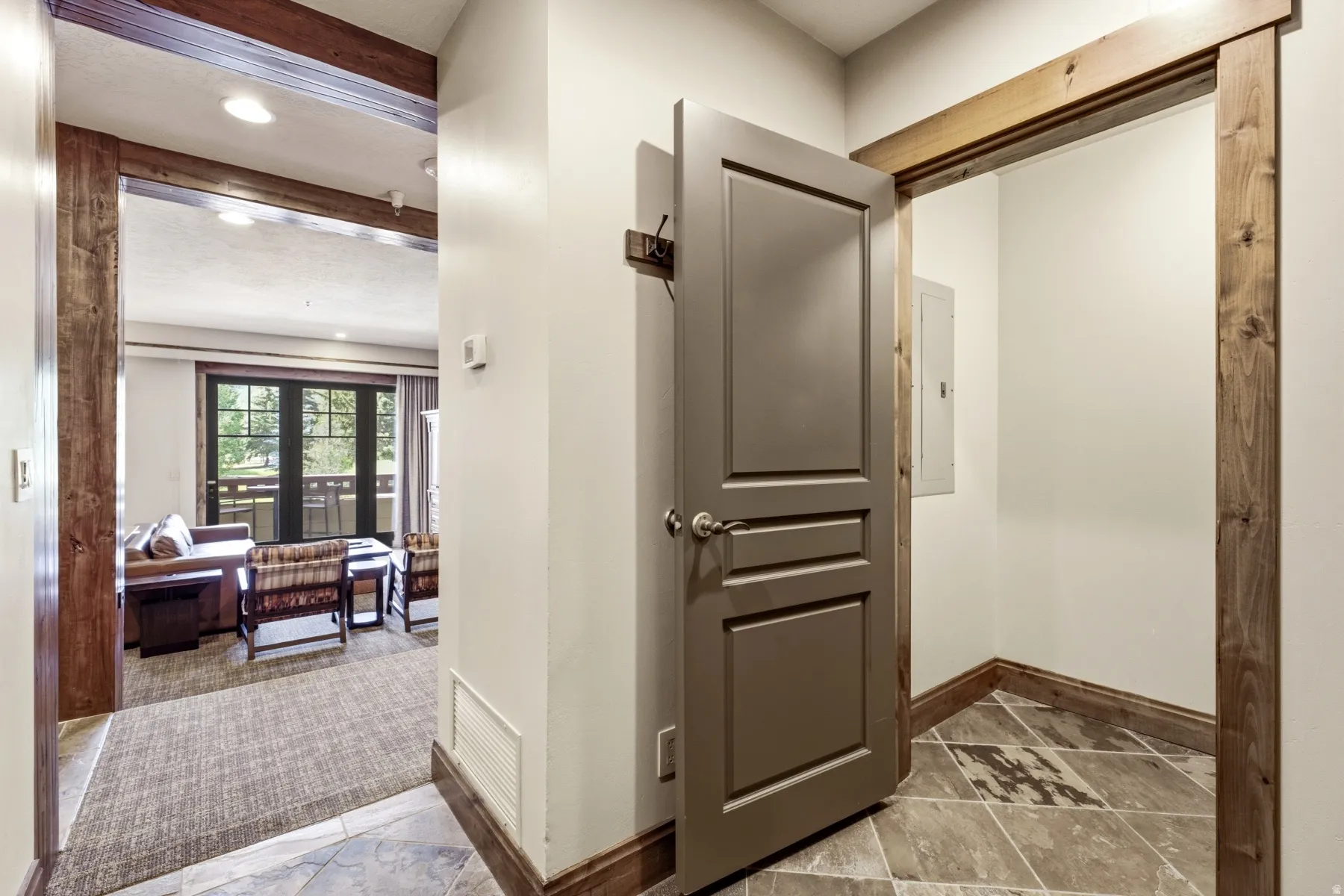 Entryway featuring patterned tile flooring and a solid panel door, opening to a living area with wood-finish trim and exposed ceiling beams