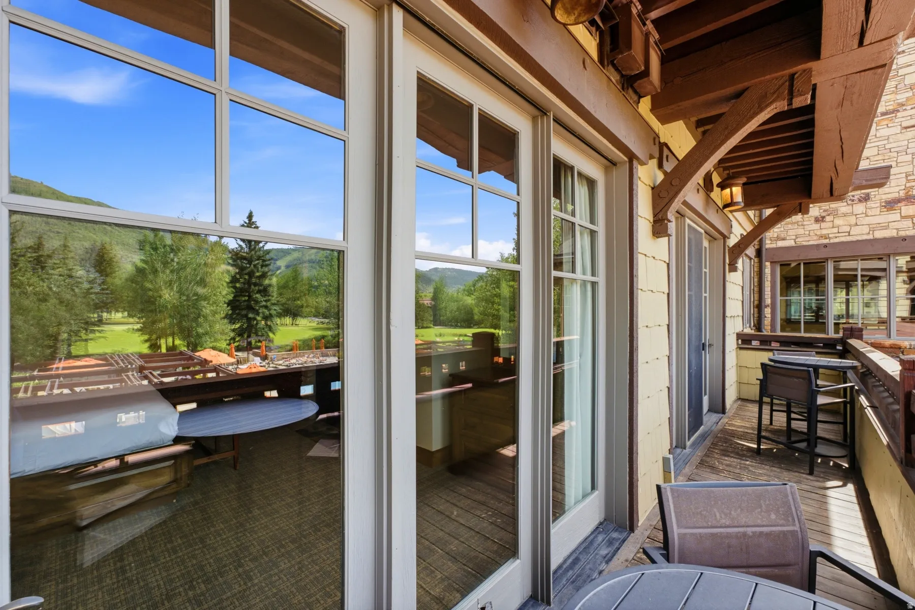 Exterior balcony featuring multiple French doors, durable decking, stone wall accents, and an overhead wooden beam structure