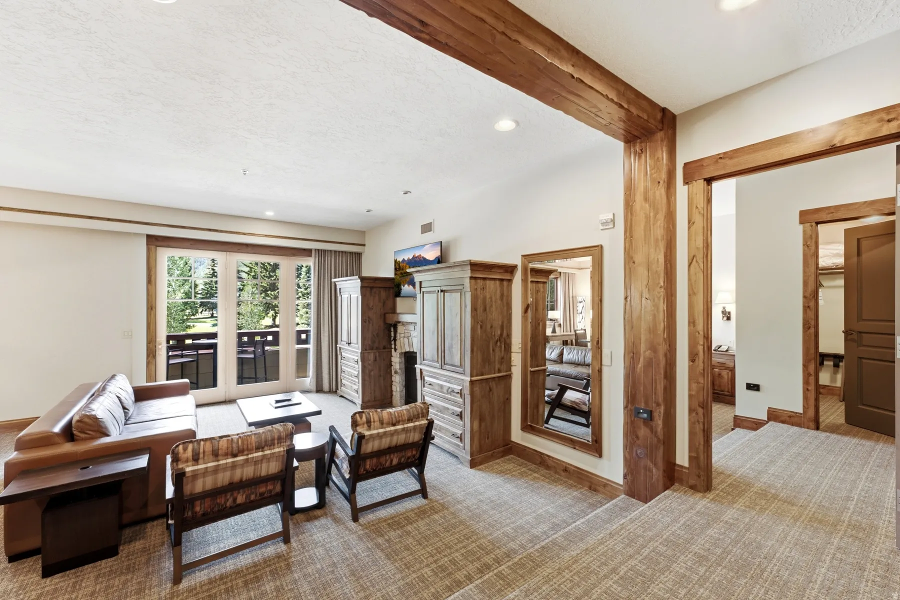 Living area featuring French doors opening to a balcony, complemented by rustic wood-finish ceiling beams and doorframes