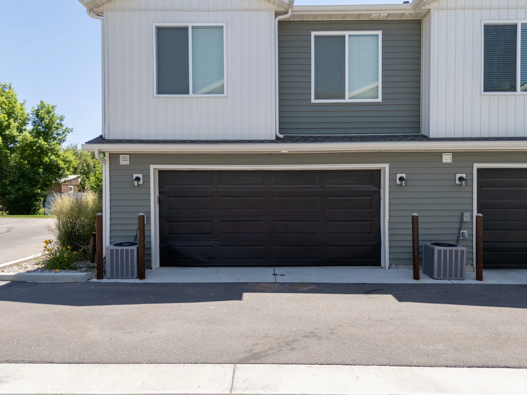 Contemporary exterior featuring two-tone siding, dark garage doors, and individual air conditioning units
