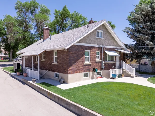 Brick exterior with a gabled roofline, front porch, concrete patio, white railing, and a manicured lawn