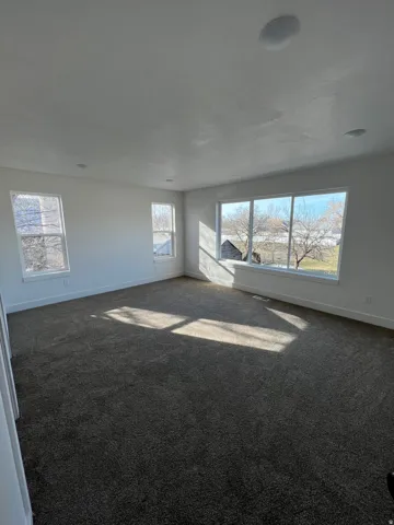 Spacious room featuring broadloom carpeting, white baseboards, and multiple windows including a large picture window