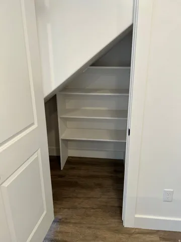 Under-stair storage area featuring multiple built-in white shelves and wood-finish flooring