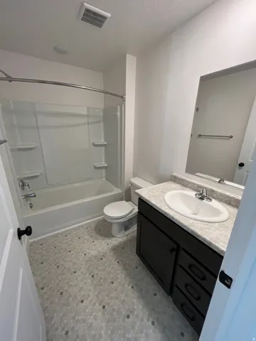 Bathroom featuring a white tub/shower combination, hexagon mosaic tile flooring, a dark wood-finish vanity with an integrated sink, a light-toned countertop, and a wall-mounted mirror