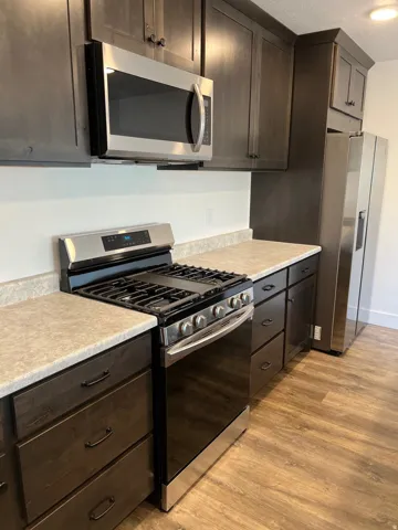 Kitchen featuring dark wood-finish cabinetry, stainless steel appliances, light-toned countertops, and wood-finish flooring