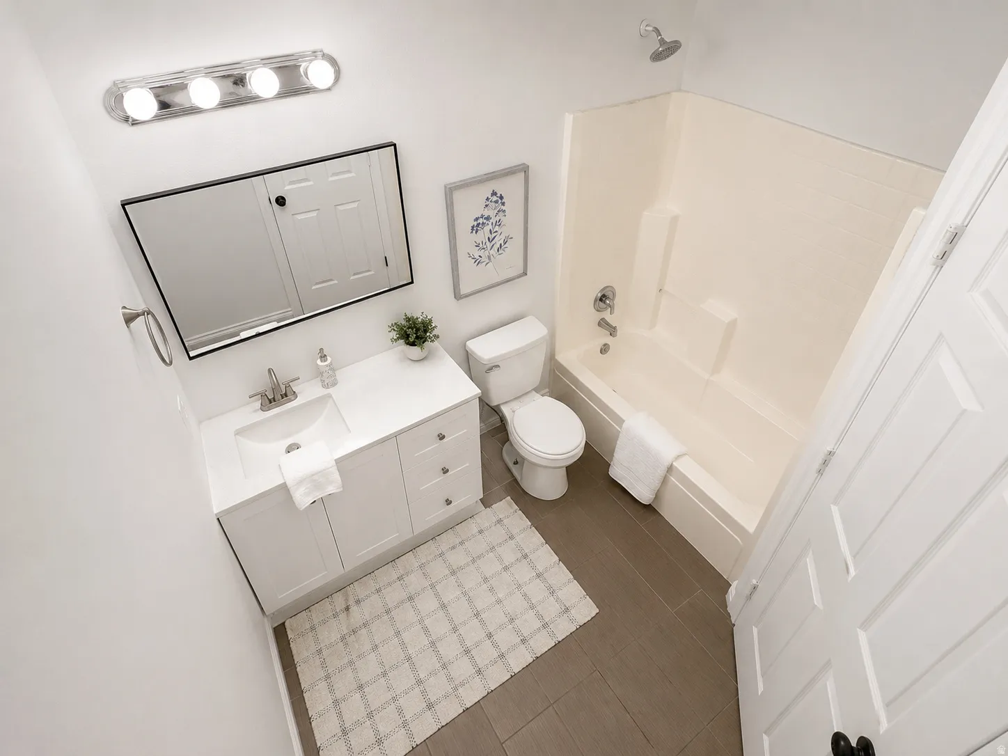 Bright bathroom featuring a single-sink vanity with white cabinetry and a rectangular mirror, a toilet, a full bathtub with an integrated shower, and dark gray tile flooring