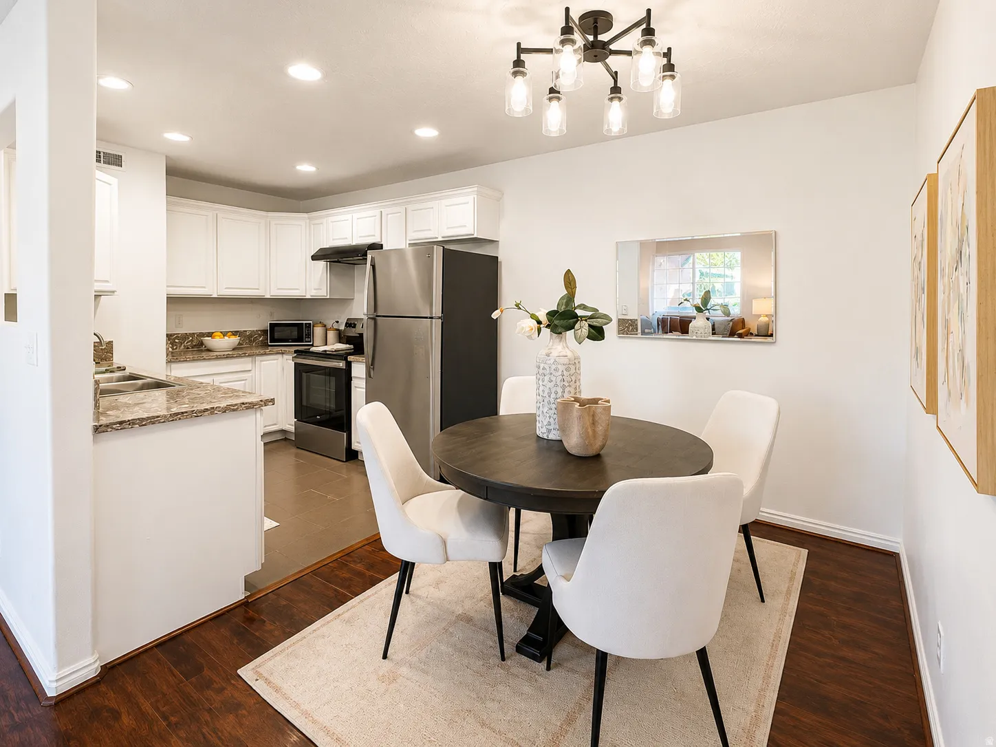 Open-concept dining area featuring a modern black chandelier, wood-finish flooring, and a kitchen with white cabinetry, granite countertops, and stainless steel appliances
