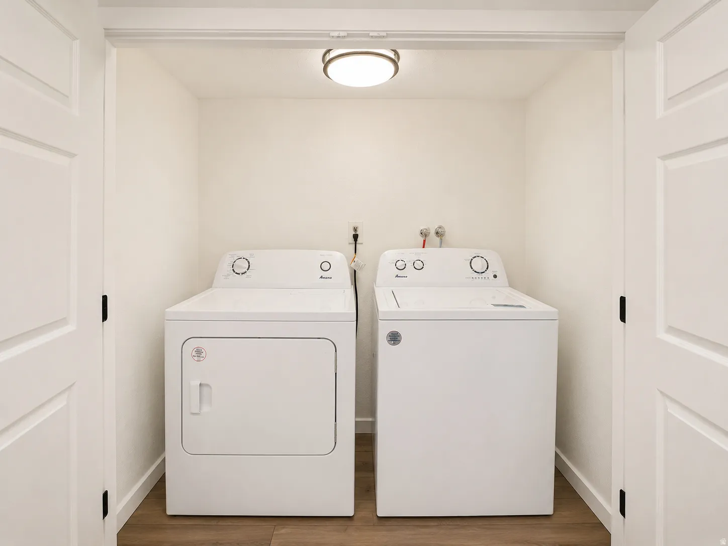 Dedicated laundry closet with wood-finish flooring, included washer and dryer, ceiling-mounted light fixture, and bifold paneled doors