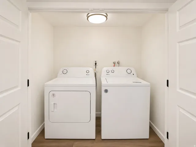 Dedicated laundry closet with wood-finish flooring, included washer and dryer, ceiling-mounted light fixture, and bifold paneled doors
