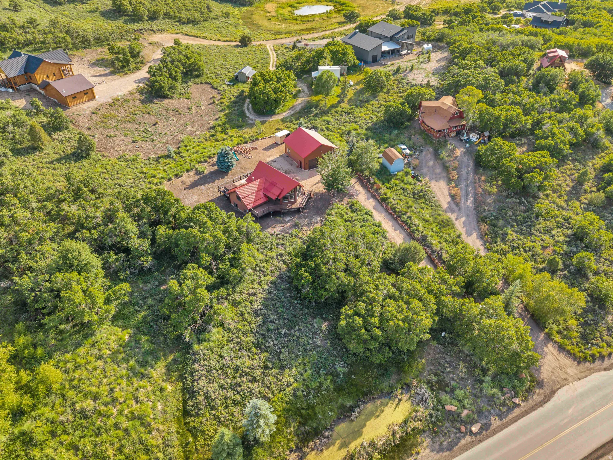 Expansive, verdant acreage featuring multiple structures, including two primary residences with red roofs and wood-clad exteriors