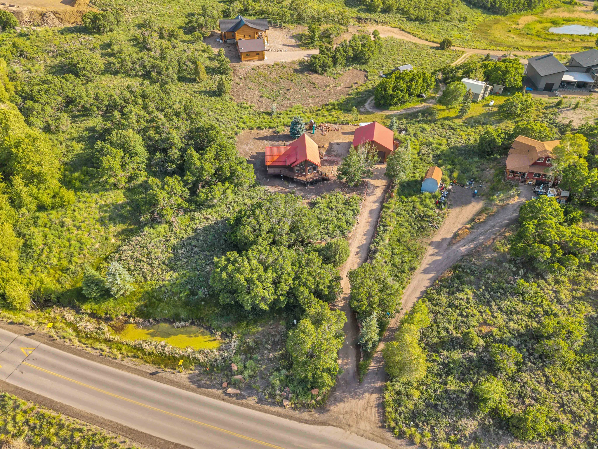 Expansive, treed acreage featuring multiple structures, including two properties with red roofs and a smaller outbuilding