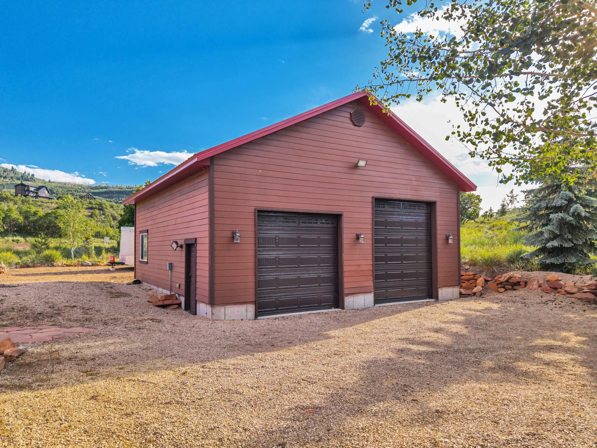 Detached two-car garage with horizontally-paneled siding, a red gable roof, and two brown sectional garage doors