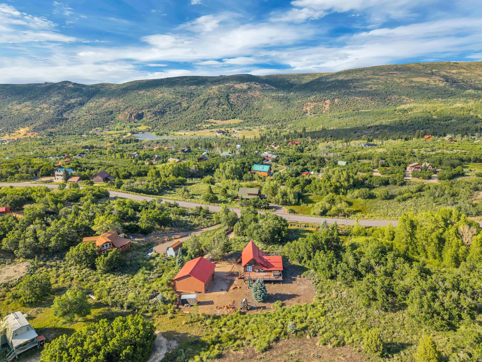 Expansive property featuring two distinct structures with red metal roofs, surrounded by dense green foliage and a mountainous backdrop
