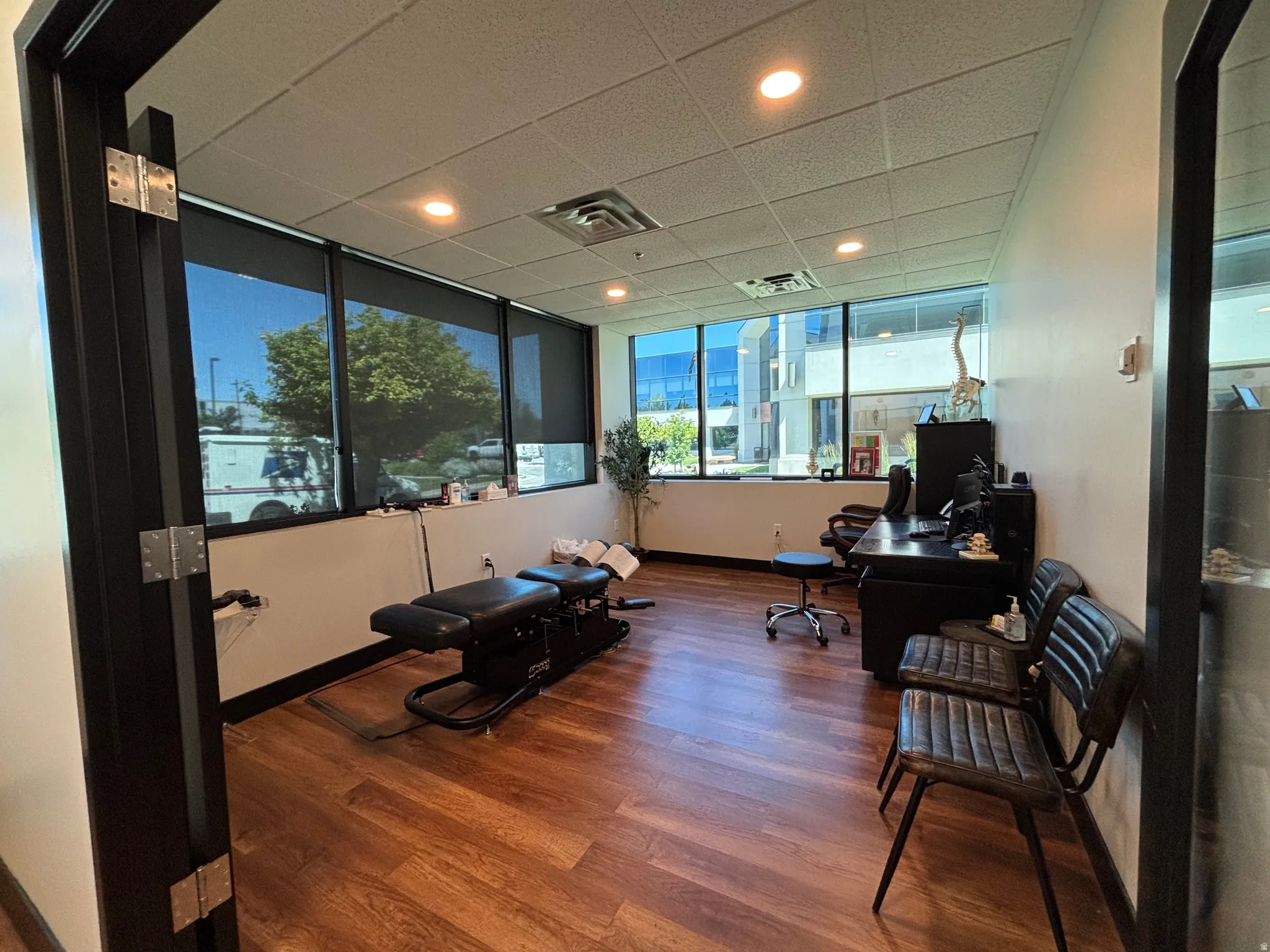Commercial space featuring wood-finish flooring, drop ceiling with recessed lighting, and expansive windows with roller shades