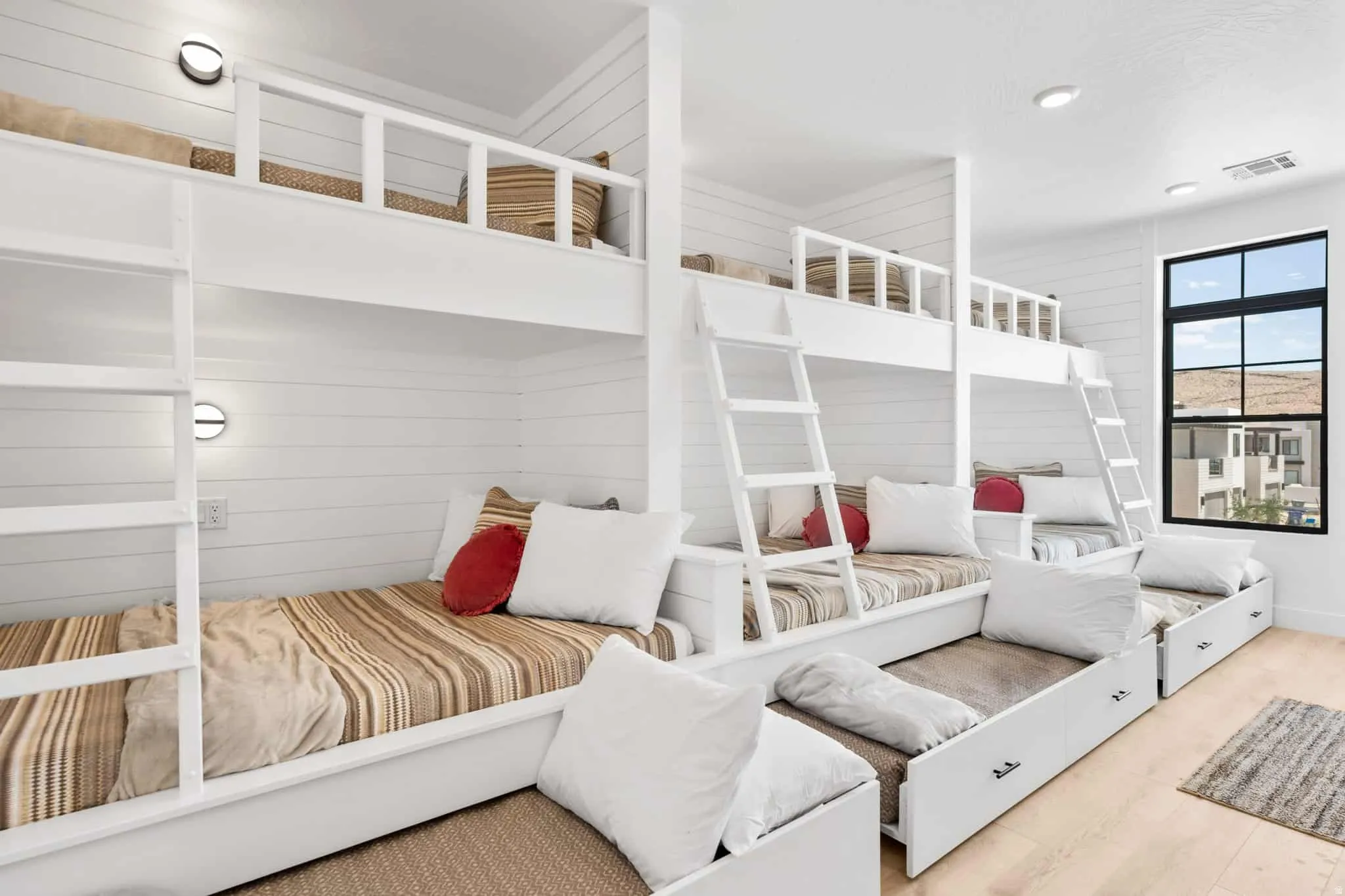 Built-in bunk beds featuring integrated lighting, shiplap wall finishes, natural wood-finish flooring, and a large black-framed window