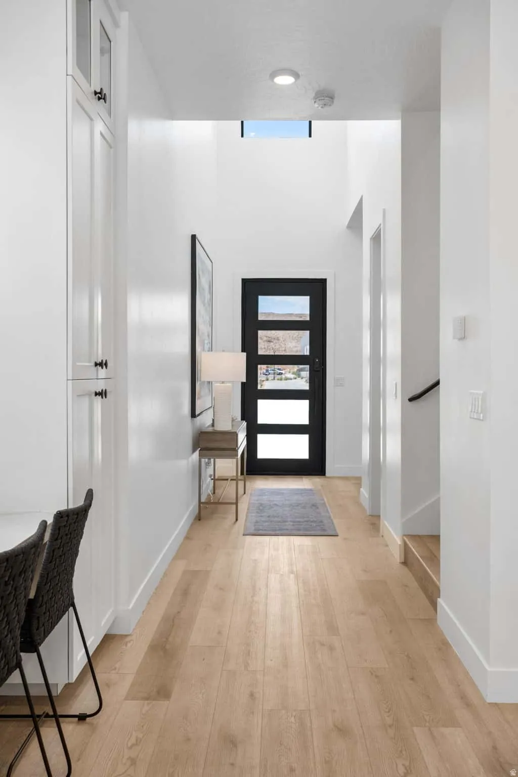 Entryway featuring wood-finish flooring, a contemporary black door with frosted glass panels, and a prominent transom window