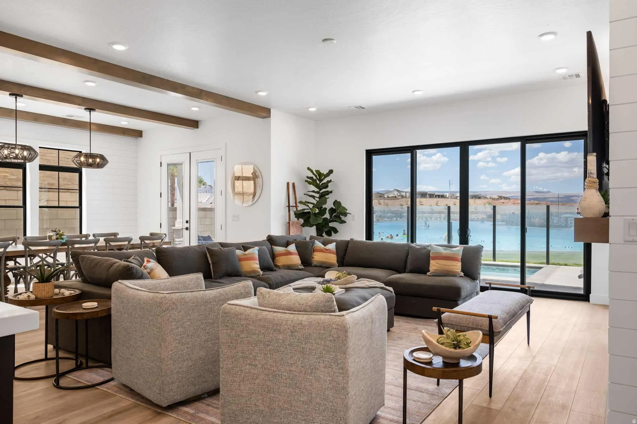 Open-concept living area featuring light wood-finish flooring, white shiplap accent wall, and exposed wood ceiling beams