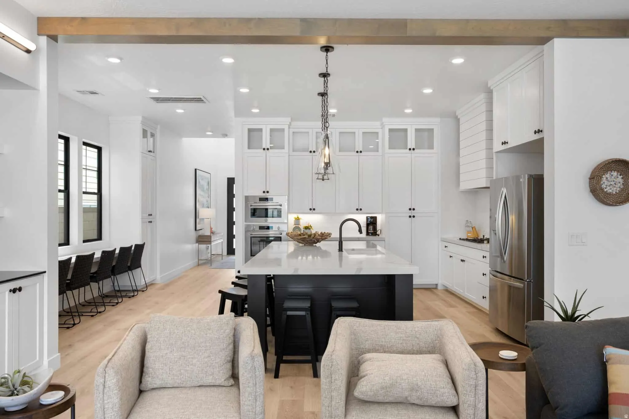 Modern kitchen featuring a large central island with seating, white shaker cabinetry, stainless steel appliances, and wood-finish flooring