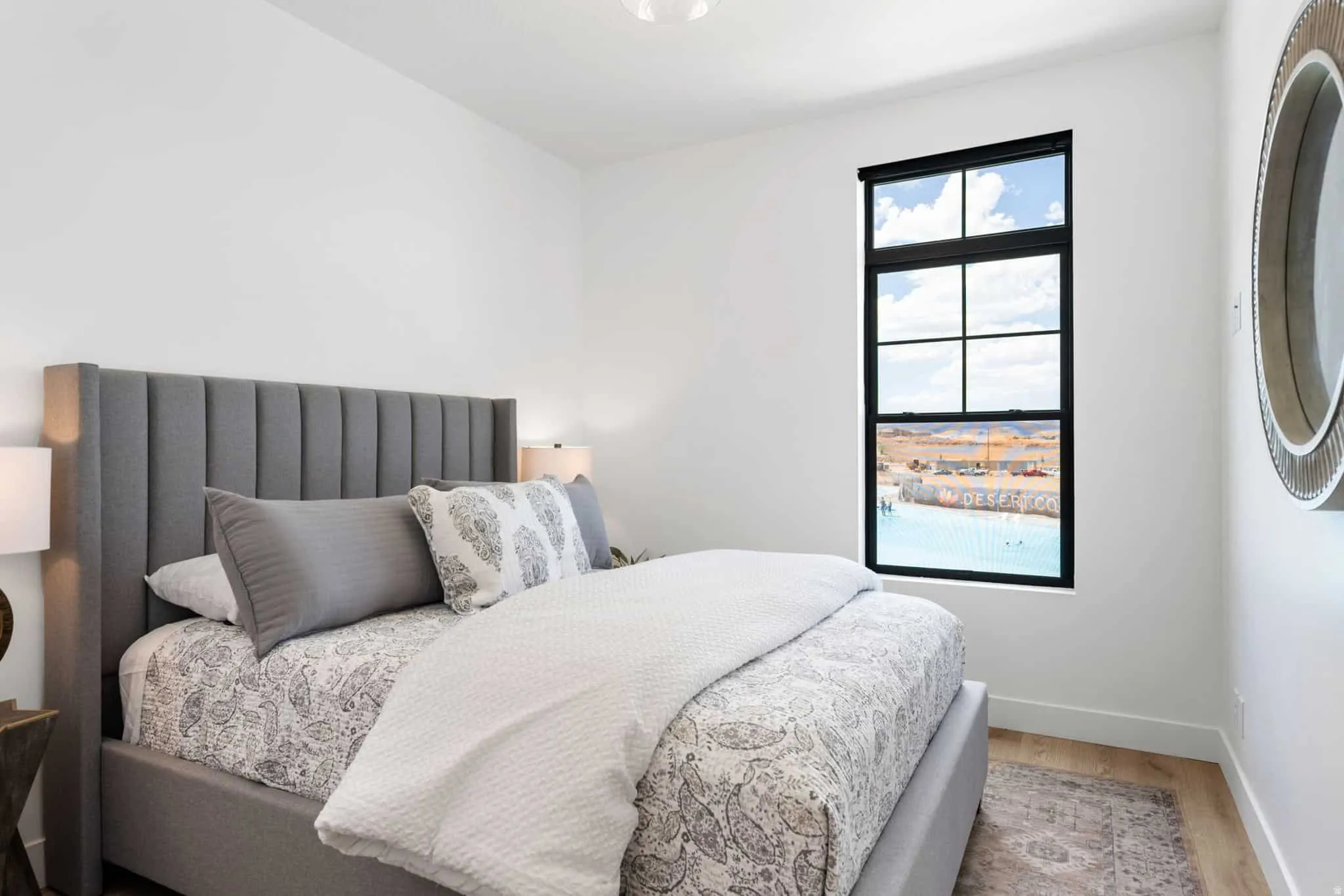 Light-filled room featuring a large black-framed window, white walls, and wood-finish flooring