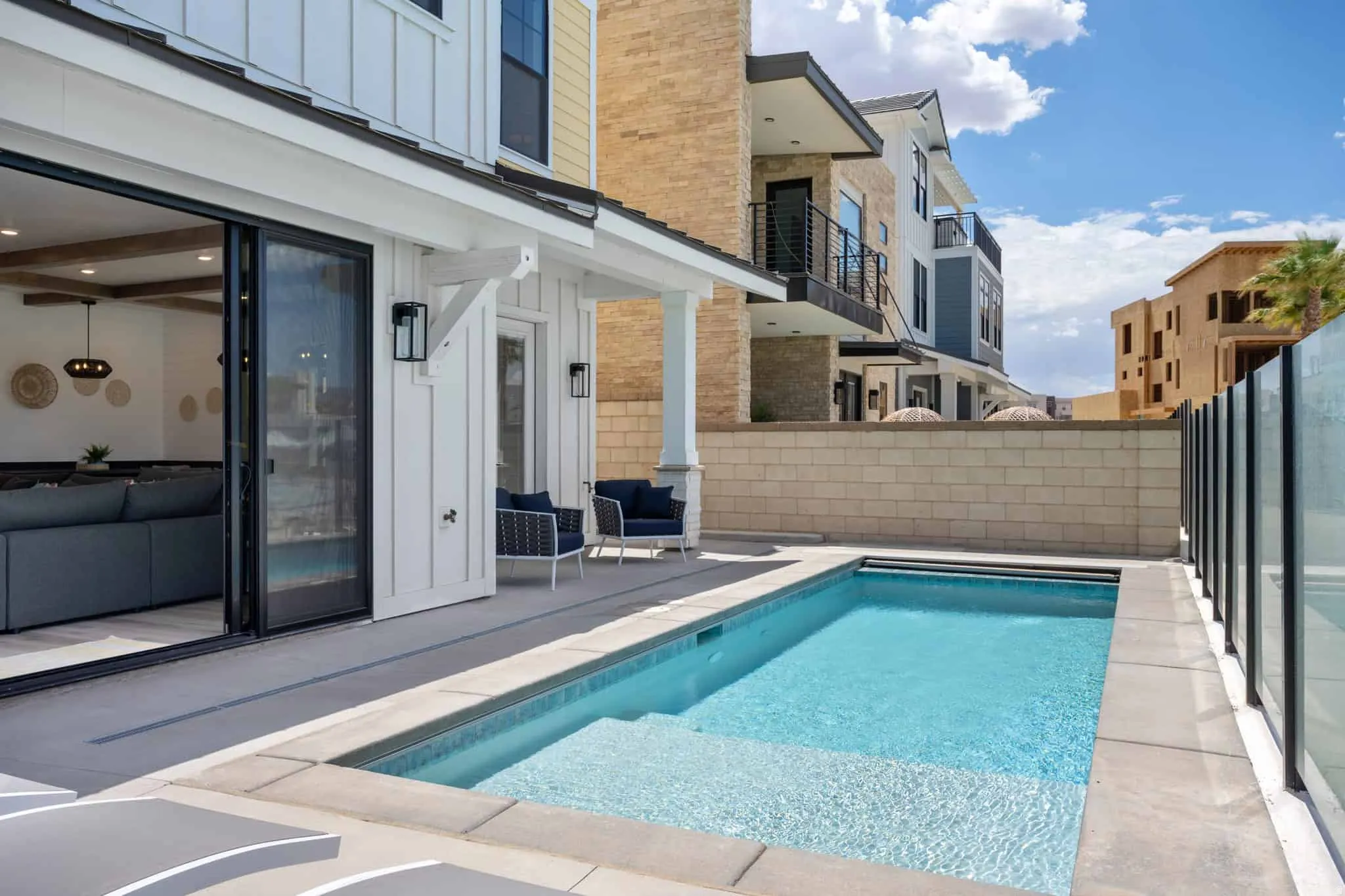 Outdoor pool with integrated steps, surrounded by a concrete patio and a glass panel fence