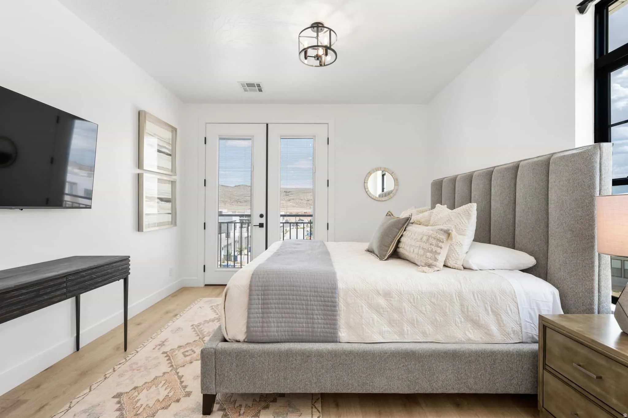 White-painted walls with wood-finish flooring, featuring a double French door leading to a balcony with black metal railing