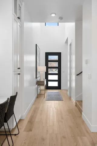 Entryway featuring wood-finish flooring, a contemporary black door with frosted glass panels, and a prominent transom window