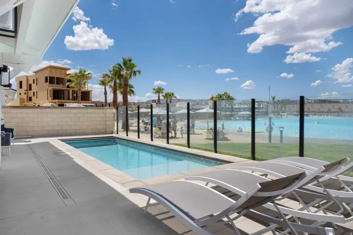 Private swimming pool with a surrounding hardscape patio, a glass panel fence, and mature palm trees