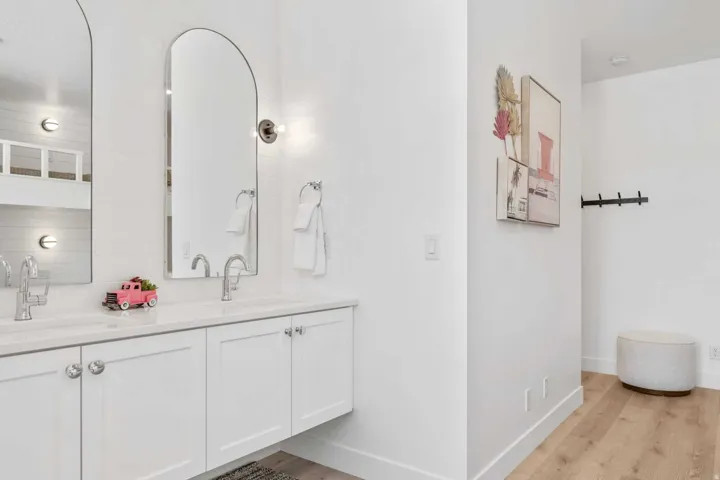 Dual vanity with white cabinetry, polished chrome hardware, and arched mirrors