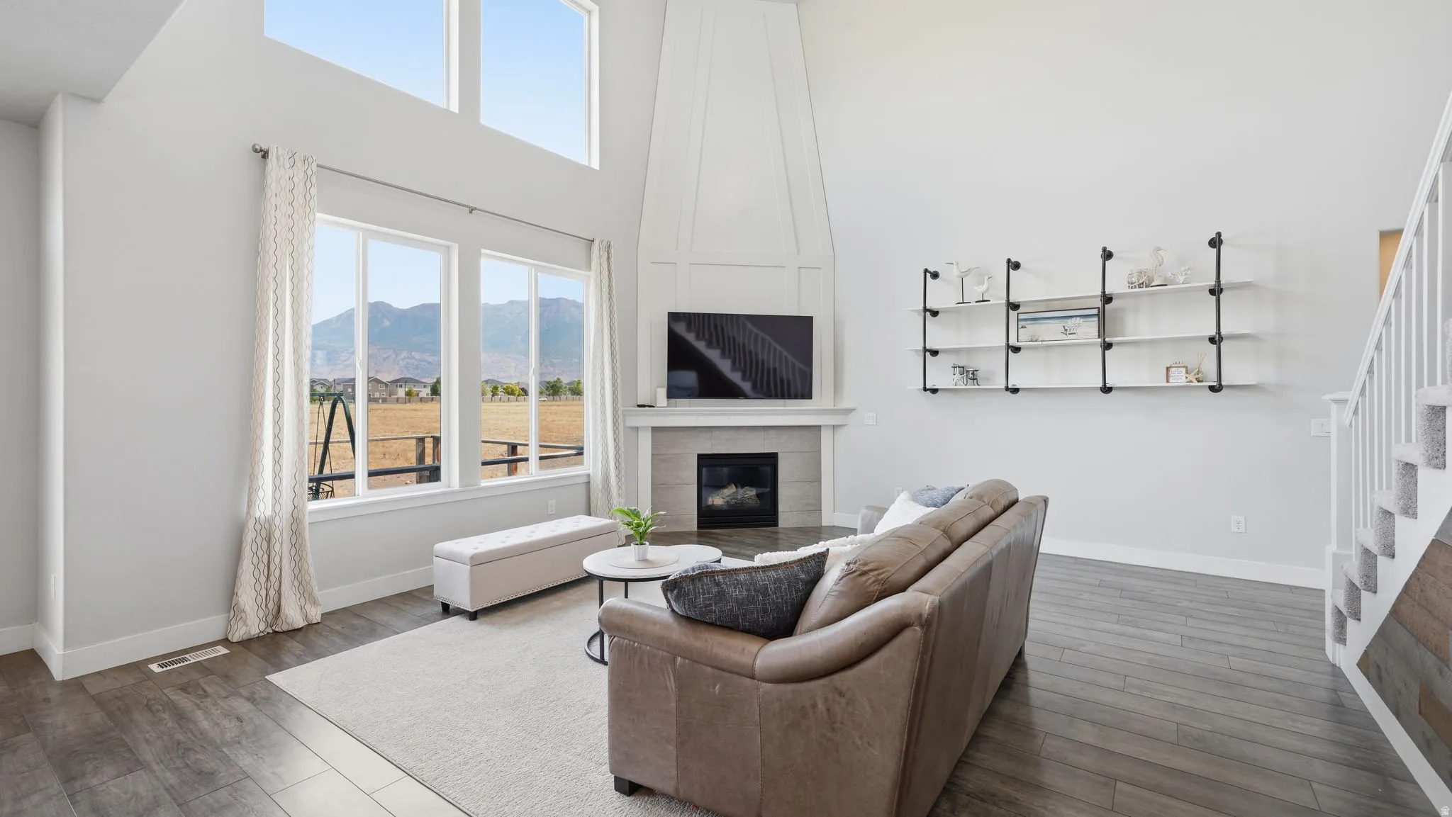 Spacious living area featuring a vaulted ceiling, large windows, wood-finish flooring, a contemporary fireplace with mantel, and built-in shelving