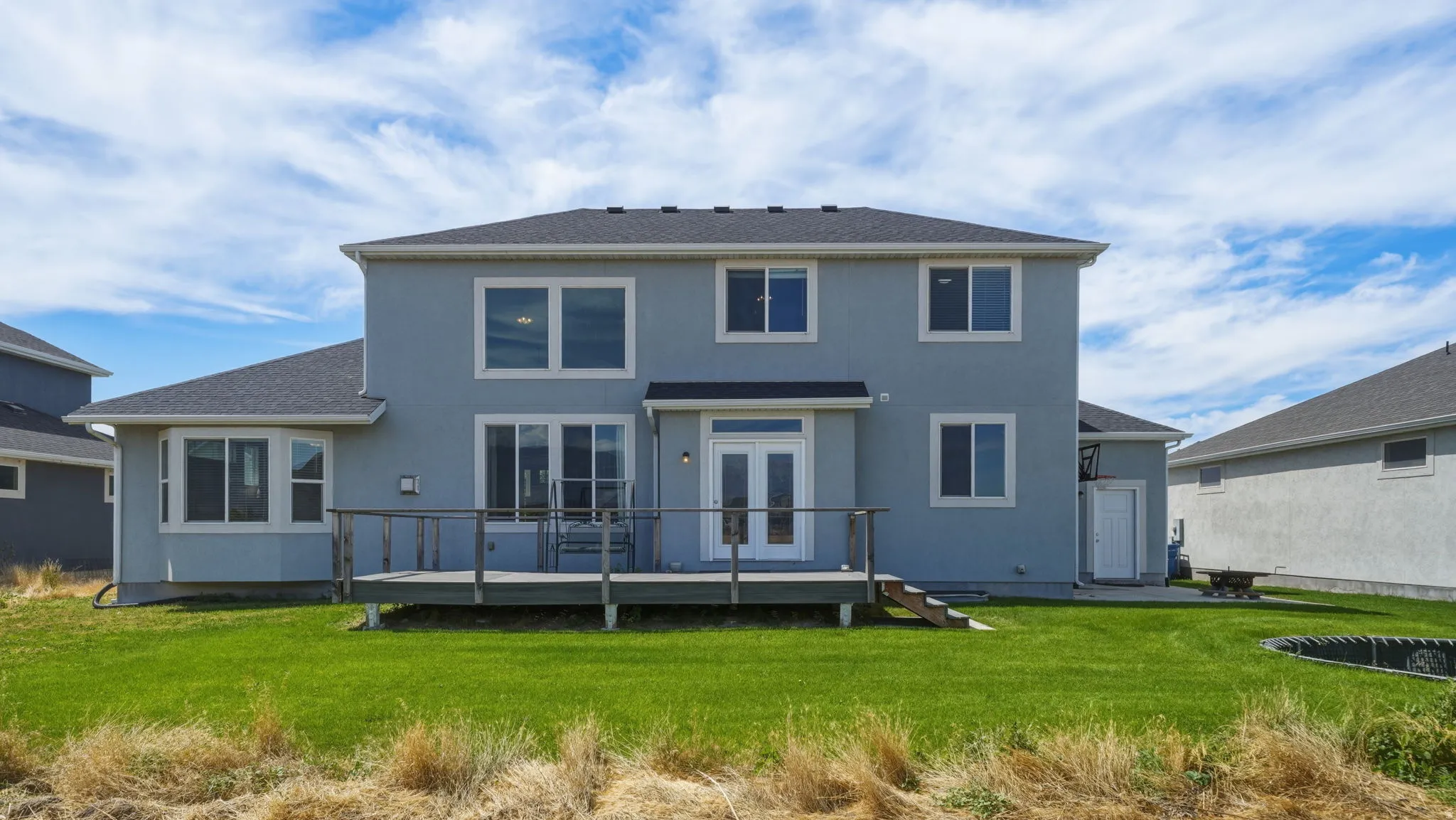 Rear exterior featuring a spacious wooden deck with railings, dual glass-paneled doors, and a bay window
