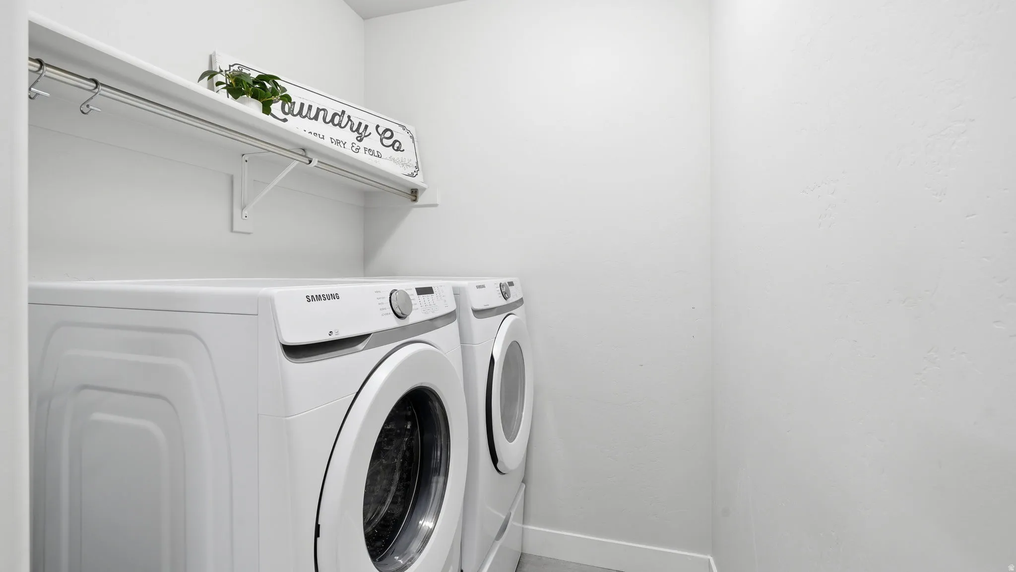 Dedicated laundry area featuring a white wall shelf with an integrated hanging rod and white walls