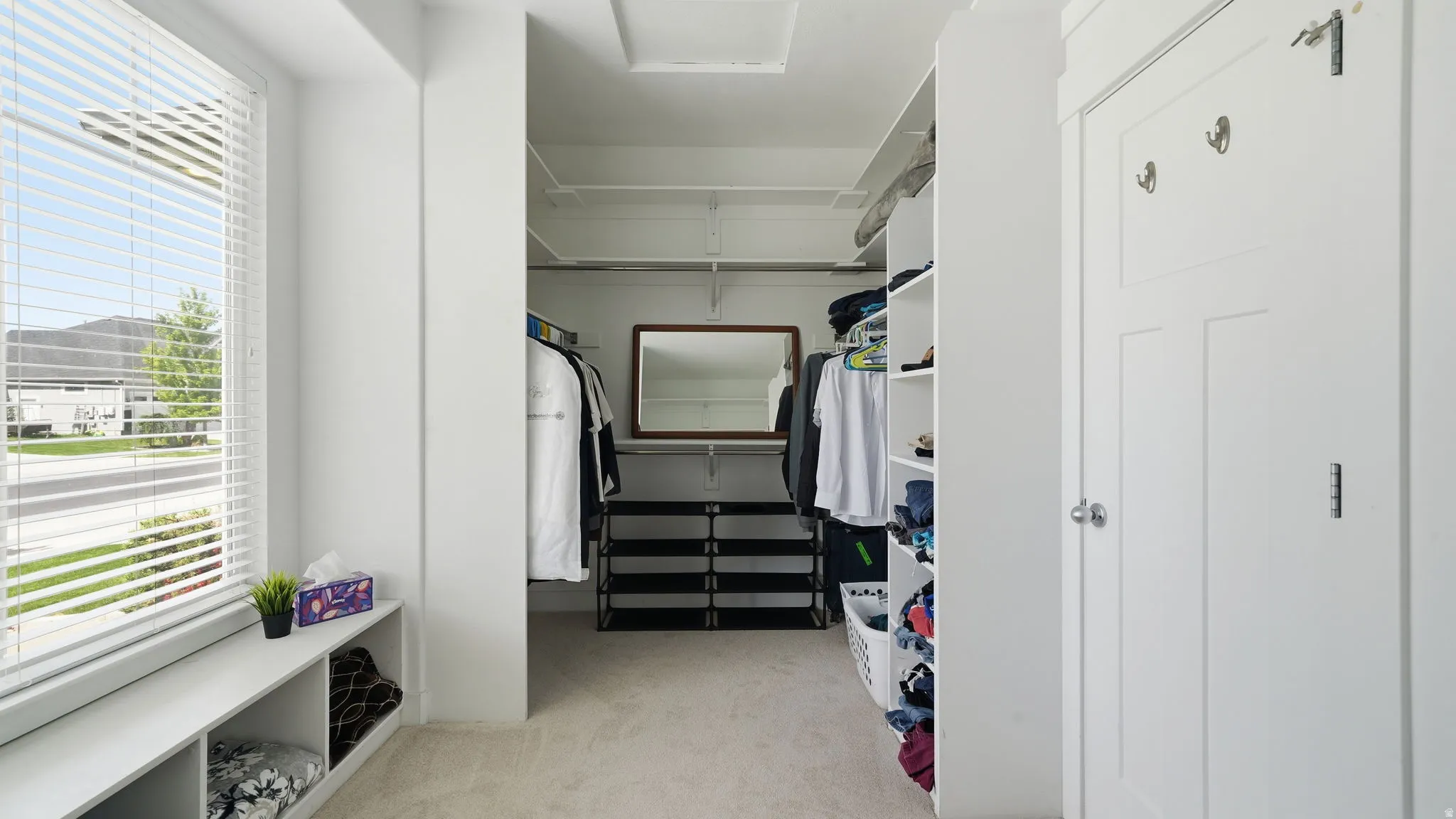 Walk-in closet featuring built-in shelving, carpet flooring, a window with blinds, and a built-in bench with cubby storage