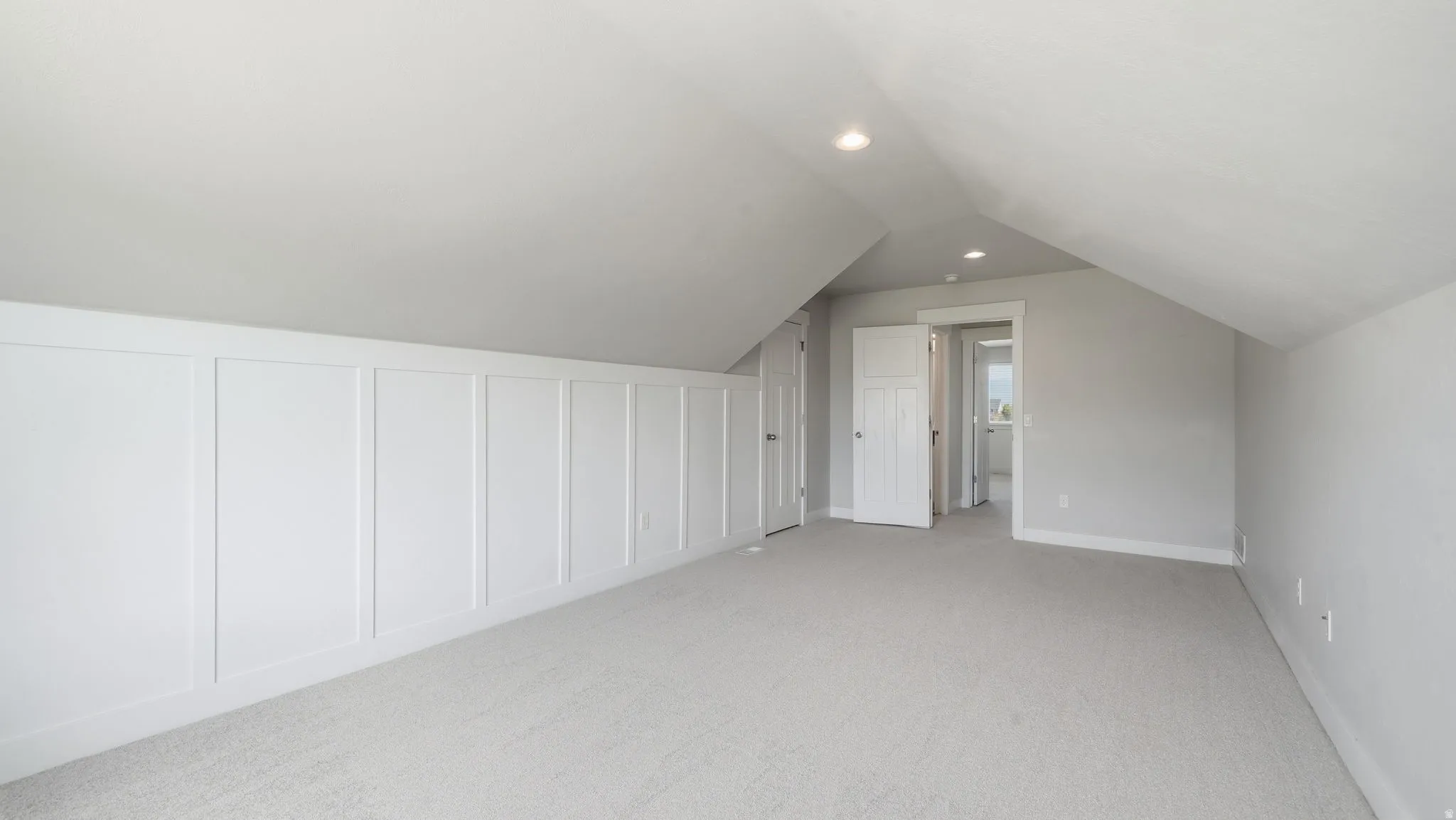 Carpeted room featuring a white paneled accent wall, recessed lighting, and a sloped ceiling