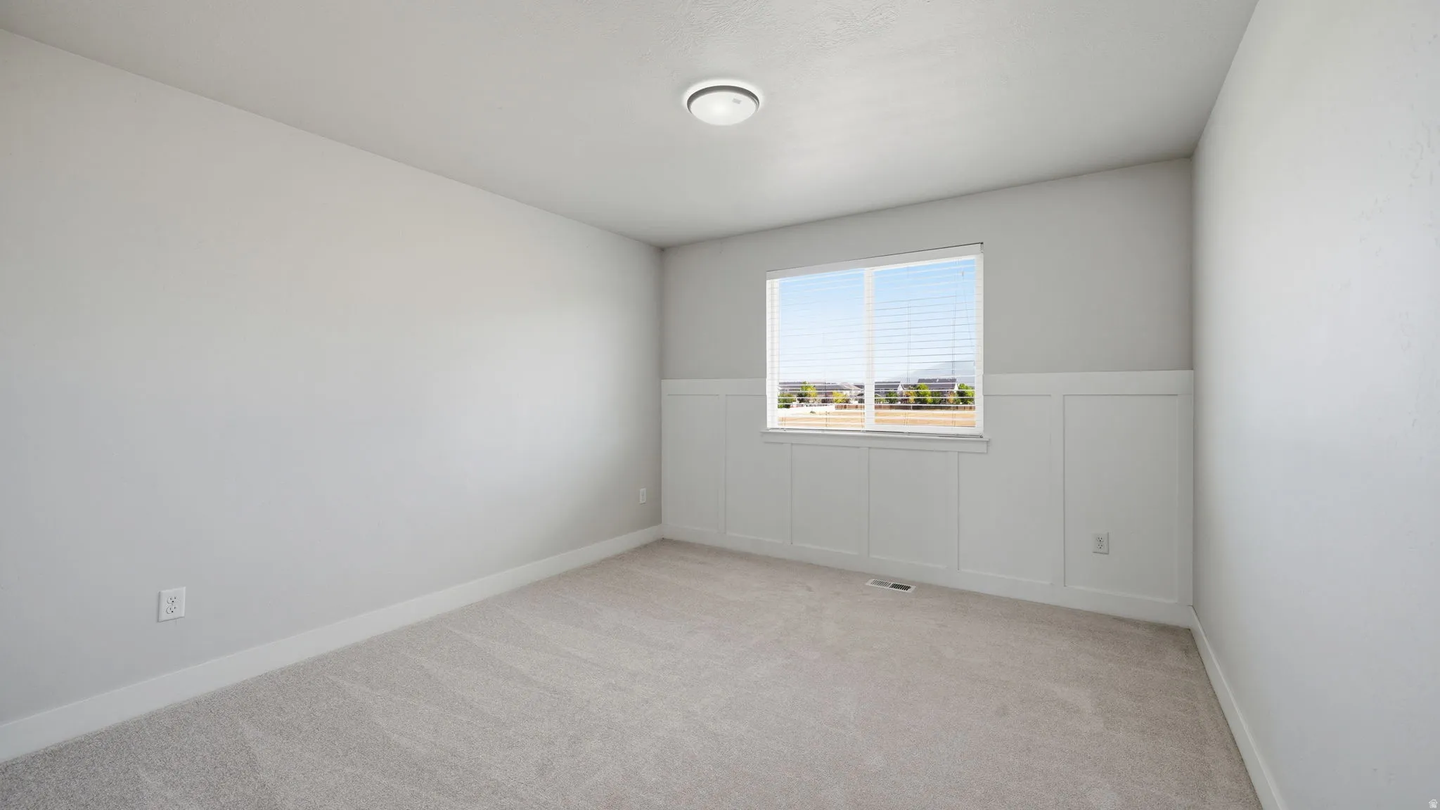 Light gray carpeted room featuring a single window with white blinds, white trim, and a contemporary ceiling light fixture