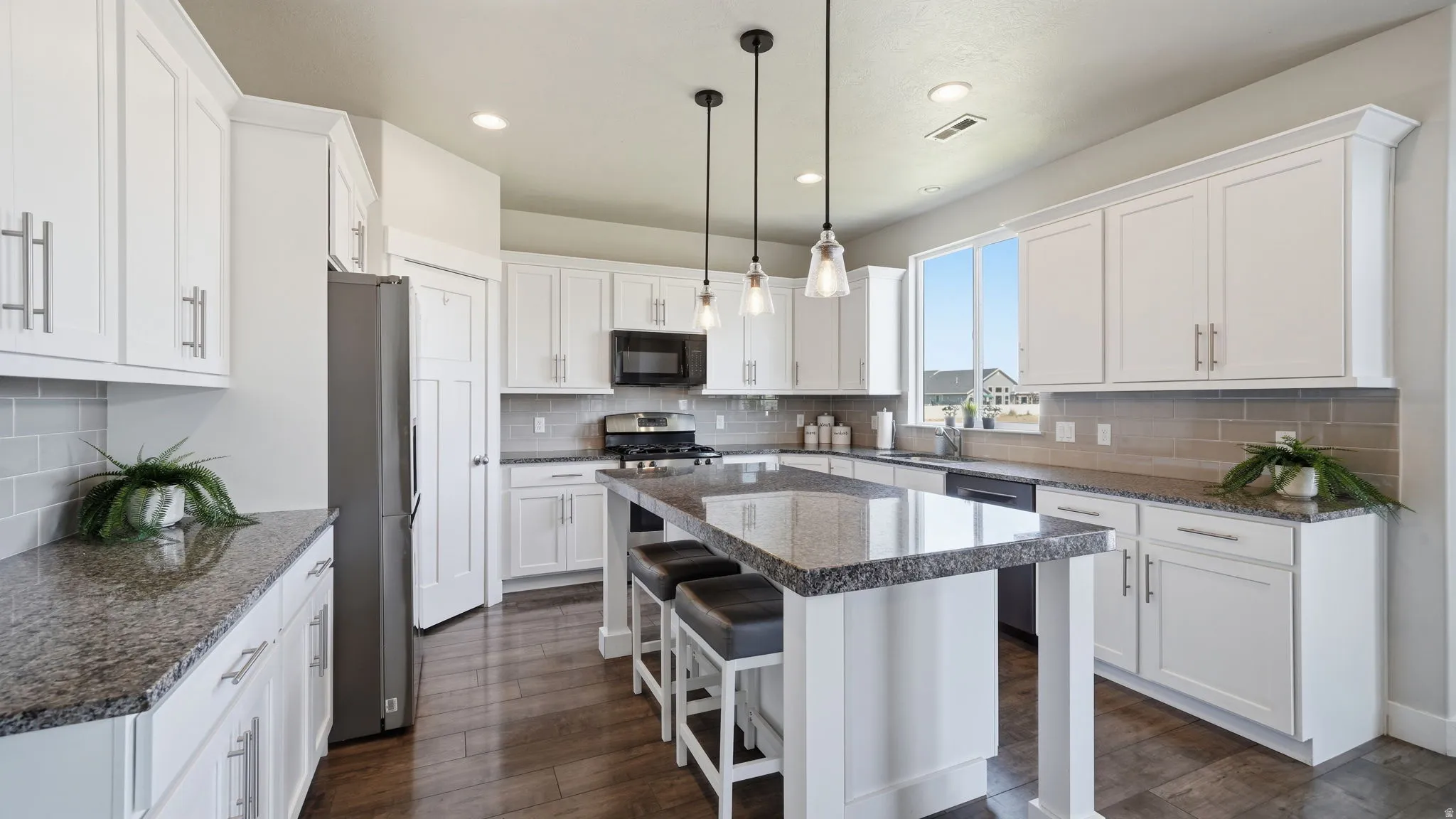 Kitchen featuring a large island with seating, white shaker cabinetry, stone-finish countertops, stainless steel appliances, and wood-finish flooring