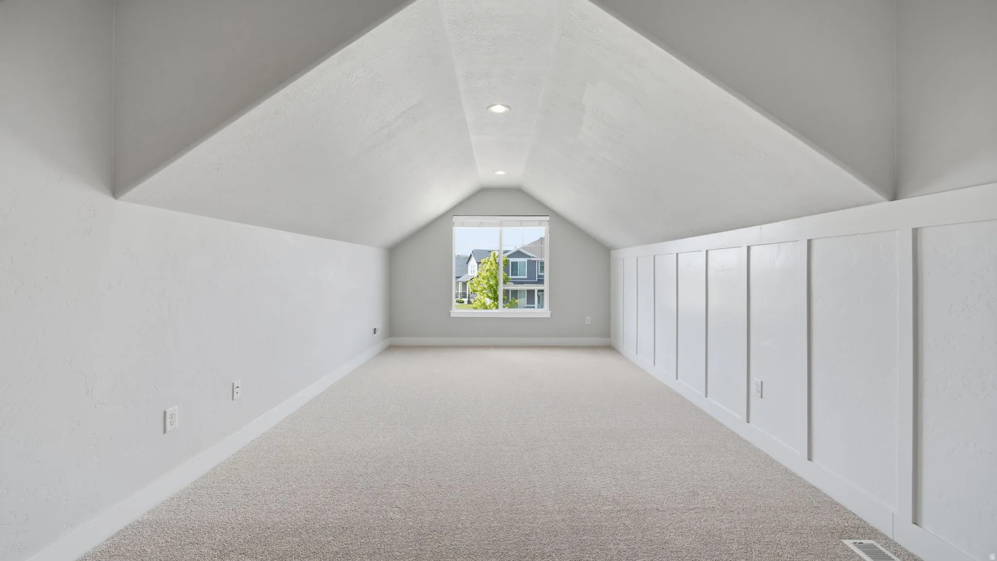 Carpeted attic space featuring a window, recessed lighting, and a paneled accent wall