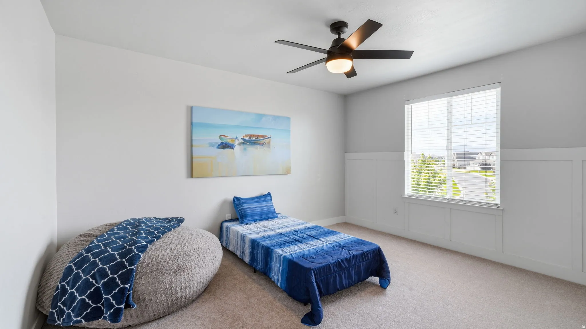 Light-filled room featuring a large window with blinds, a ceiling fan with integrated lighting, board and batten wall detailing, neutral carpeting, and light gray wall paint