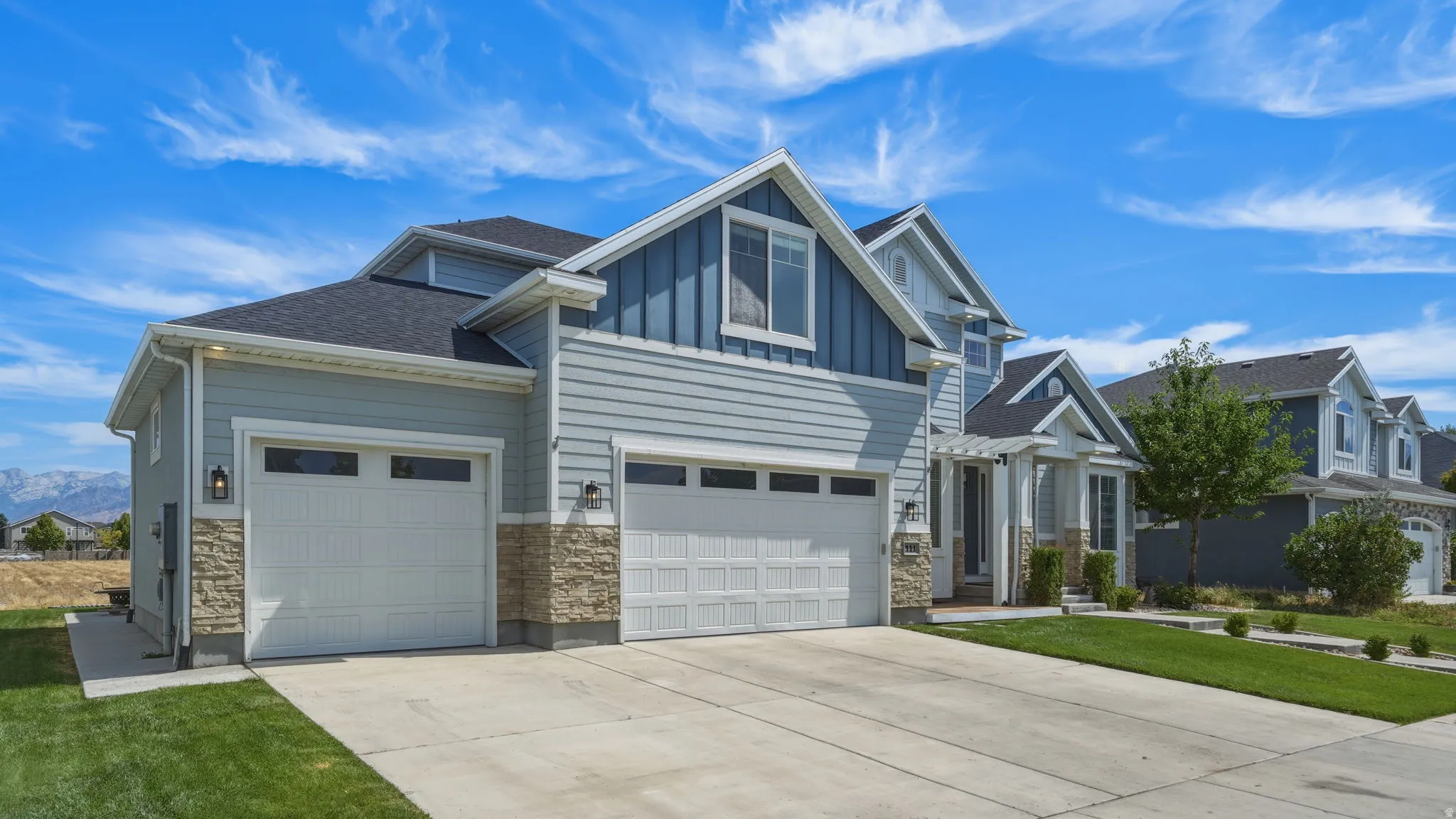 Two-story residence featuring light blue siding, stone veneer accents, and a dark shingle roof