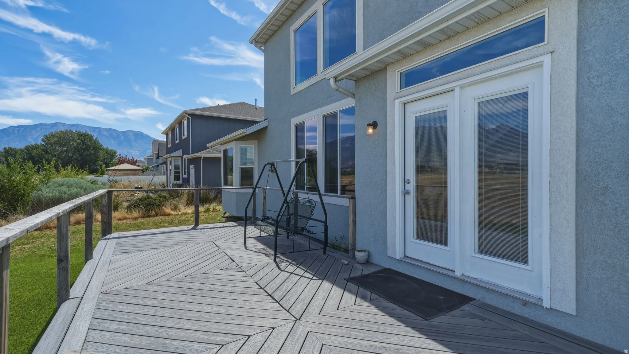 Spacious wood-finish deck with railing, featuring double glass doors with transom window, and a stucco exterior