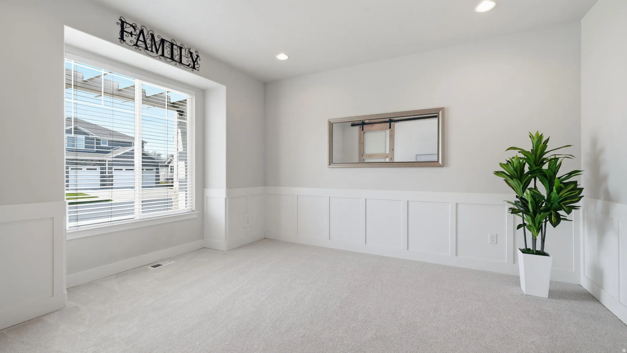 Bright interior space featuring a large window, light-colored carpeting, white wall paneling, and recessed lighting
