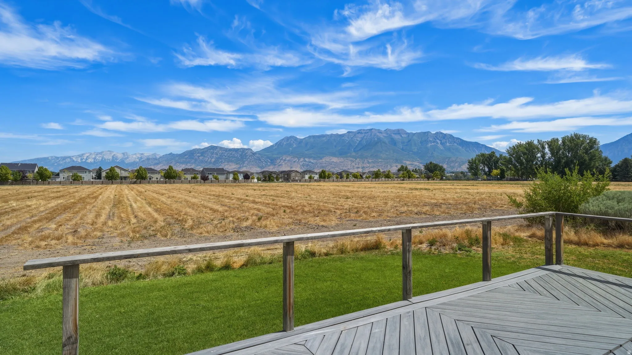 Spacious outdoor deck featuring a patterned wood-finish surface, a wooden railing, and a manicured lawn area