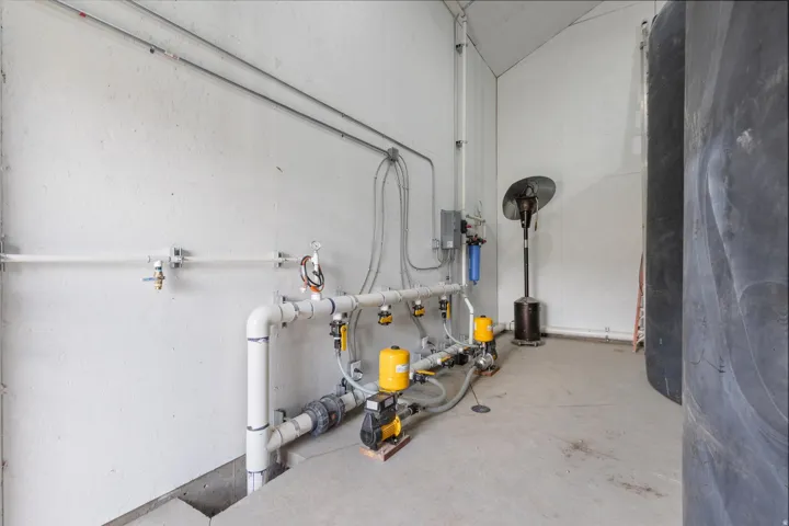 Utility room featuring exposed piping, water filtration system, pressure pumps, and a large storage tank