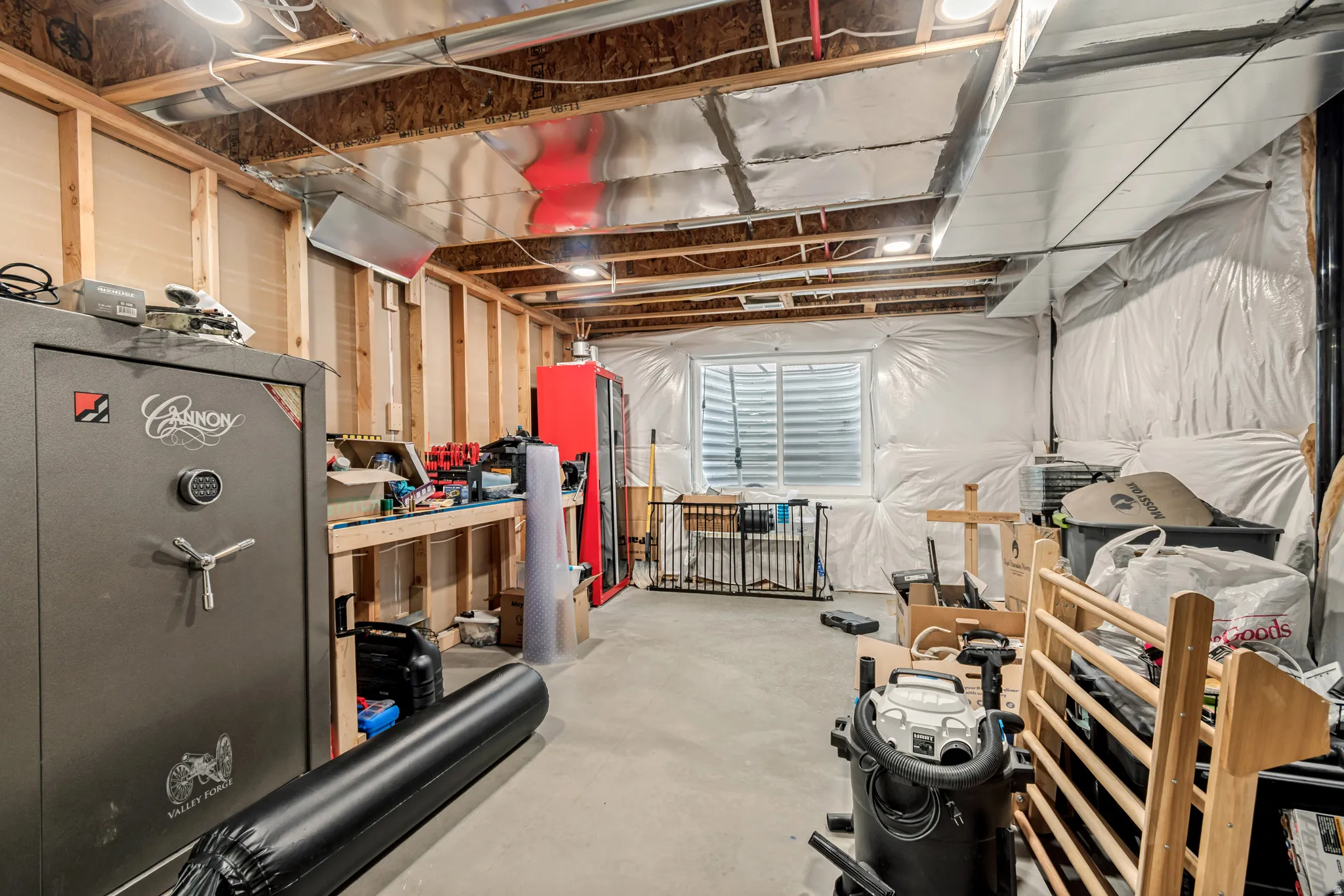 Unfinished basement space featuring exposed wooden joists, concrete flooring, perimeter insulation, a built-in workbench, and an egress window