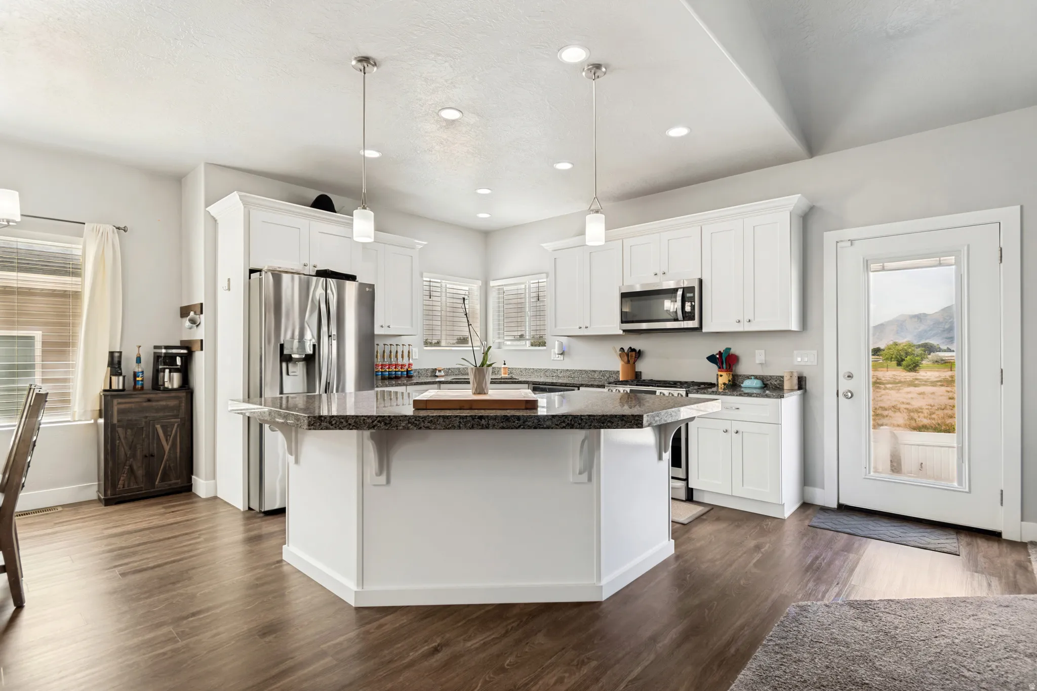 Kitchen featuring a large multi-sided island with a stone countertop, white cabinetry, stainless steel appliances, and wood-finish flooring