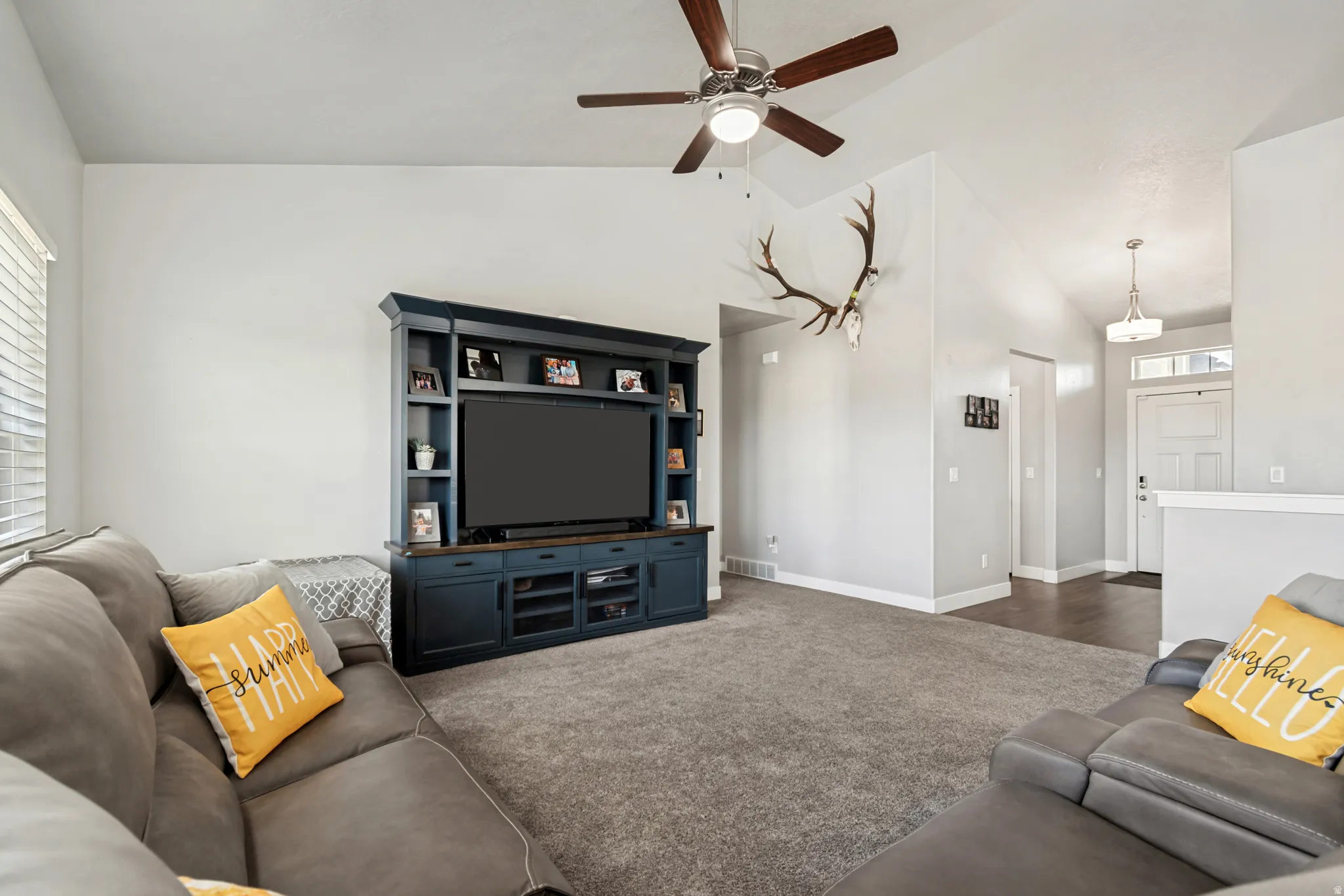 Spacious living area featuring vaulted ceilings, a ceiling fan with integrated lighting, and plush carpeting