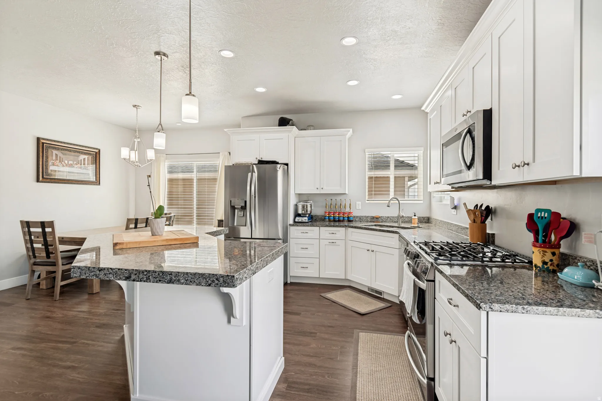 Kitchen featuring white cabinetry, stainless steel appliances, granite countertops, a center island with pendant lighting, and wood-finish flooring